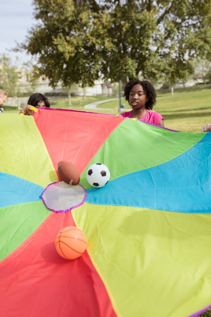 Kids enjoy outdoor play with a colorful parachute and balls on a sunny day in the park.